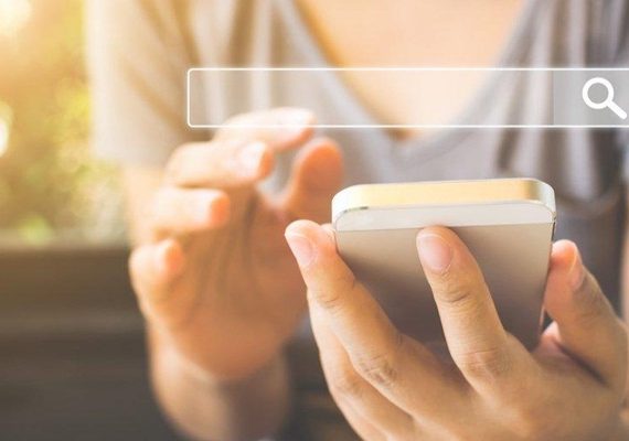 Parte do corpo de uma pessao aparecendo, com foco nas mãos, ela tem um smartphone na mão esquerda, ela está buscando como escolher as palavras-chave certas para seu site aparecer no Google.